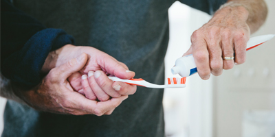 A close up of a man holding a toothbrush and another man putting toothpaste on the bristles.